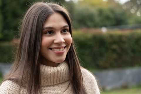 Smiling woman wearing beige turtleneck, looking right in garden, lifestyle portrait
