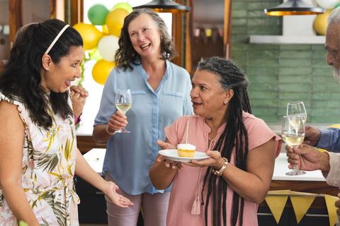 Multigenerational friends celebrating birthday in kitchen holding cupcake and toasting wine