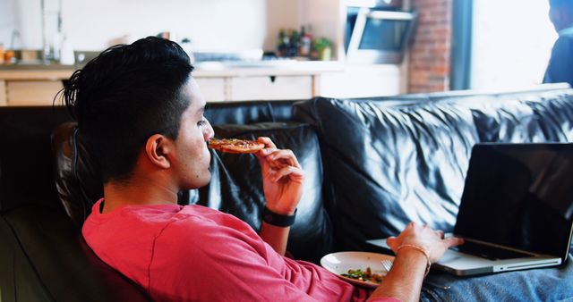 Young man eating pizza while working from home on laptop - Download Free Stock Images Pikwizard.com