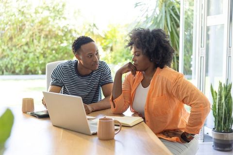 African american couple working together at sunlit home table with laptop and notes