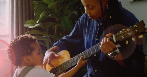 Mother Guiding Child Playing Guitar in Sunlit Living Room