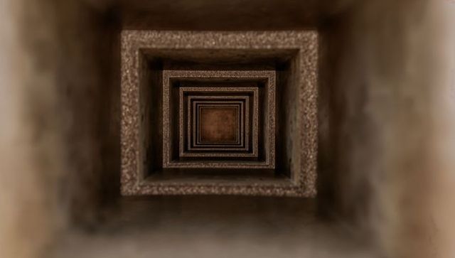 Receding square shaft revealing endless symmetry in dusty vertical industrial tunnel