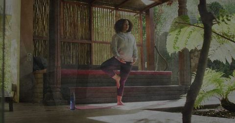 Woman practicing tree pose on pink mat under pergola in sunlit garden deck