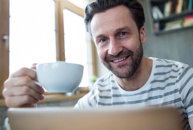 Smiling man holding a cup of coffee in coffee shop - Download Free Stock Photos Pikwizard.com