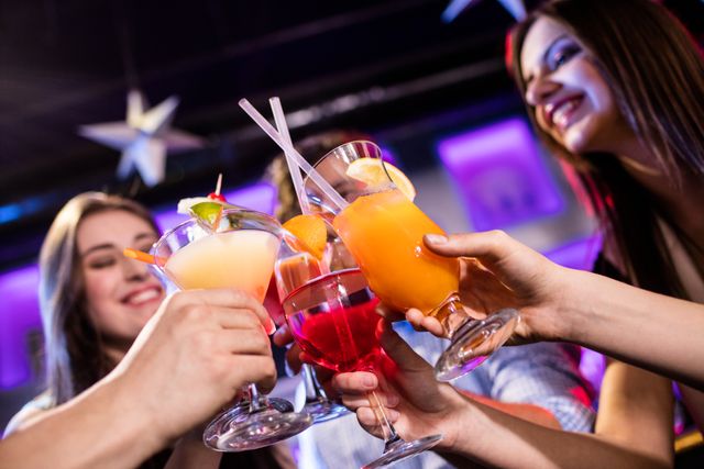 Group of friends enjoying a night out, toasting with colorful cocktails at a bar. Perfect for illustrating nightlife, social gatherings, celebrations, and festive occasions. Ideal for use in advertisements, social media posts, and articles about socializing, parties, and bar culture.