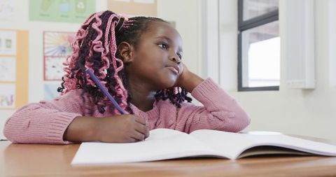 Thoughtful Student Writing in Classroom Notebook