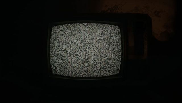 Vintage CRT television glowing with dense gray static, dark interior, peeling wall texture