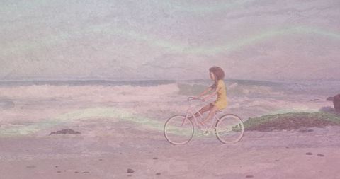 Woman in yellow dress riding pastel bicycle along beach