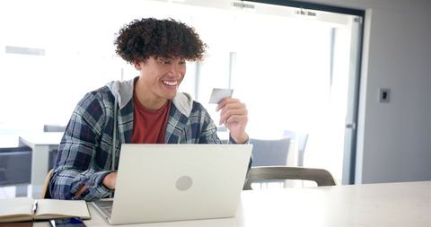 Young Man with Curly Hair Shopping Online with Laptop and Credit Card - Download Free Stock Images Pikwizard.com