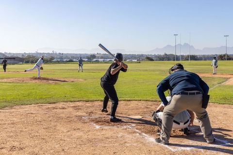 Baseball batter swinging as pitcher delivers fastball on sunny field with umpire