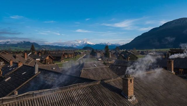 Alpine rooftops forming repeating lines with smoking chimneys and snowcapped peaks