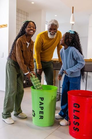 African american grandfather teaching recycling to granddaughters in bright kitchen
