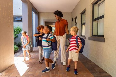 Teacher leading smiling elementary students through school corridor with backpacks