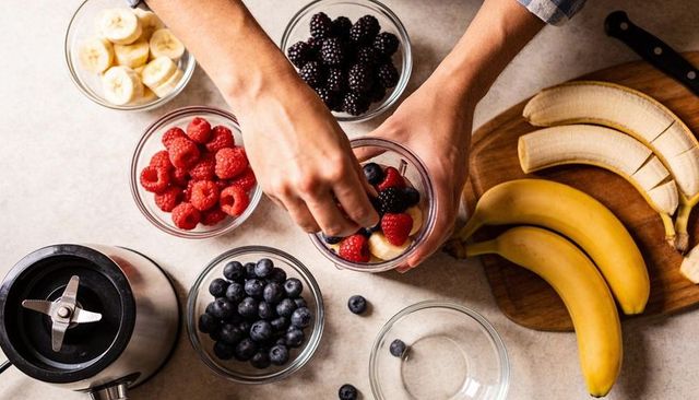 Overhead hands assembling mixed berry and banana smoothie ingredients