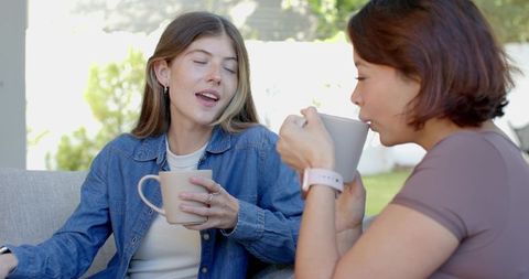 Two women sharing coffee and chatting on sunny patio, casual outdoor friendship moment