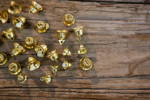 Golden Christmas bells scattered on a rustic wooden plank. Ideal for holiday-themed designs, festive invitations, Christmas cards, seasonal advertisements, and decoration ideas.