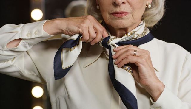Elegant senior adjusting navy and white silk neck scarf at dressing room vanity closeup