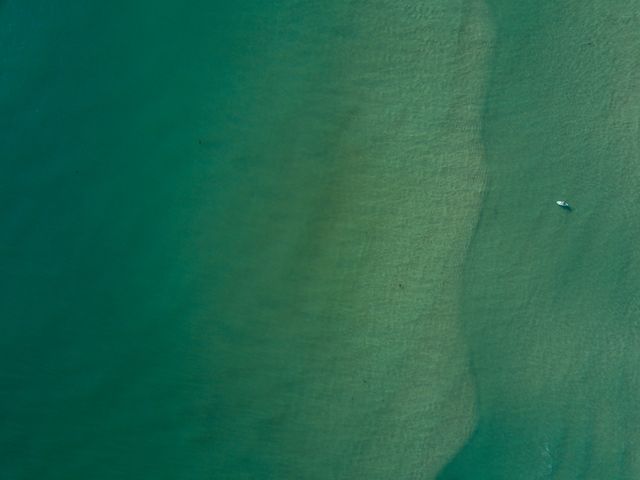Aerial view captures calm, green ocean waters, with a small lone boat floating towards the right. Ideal for visuals promoting tranquility, marine preservation, travel destinations, or individual mindfulness themes. Perfect for websites, nature postcards, ocean conservation campaigns, and travel blogs featuring coastal scenery.
