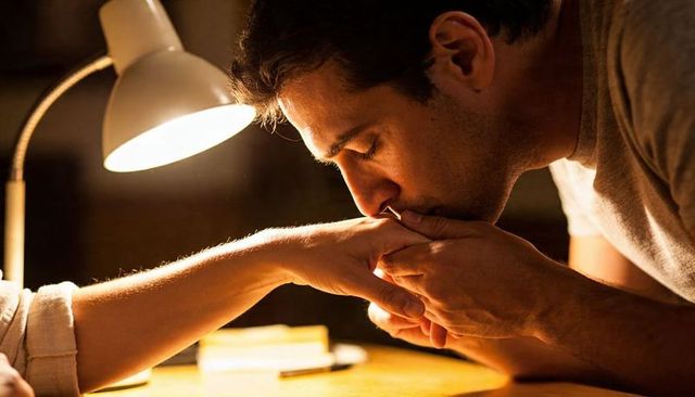 Man kissing partner's hand under warm desk lamp glow, intimate romantic moment
