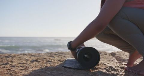 Woman Unrolling Yoga Mat by Ocean Shore at Sunrise
