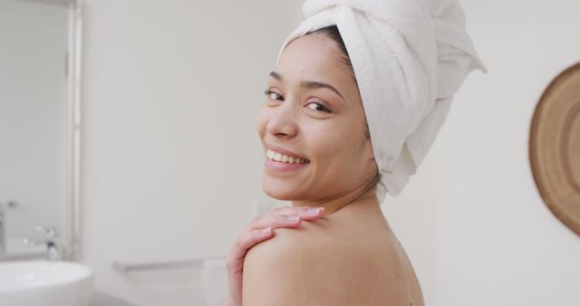 Portrait of biracial woman with towel smiling in bathroom. Beauty, health and female spa home concept.