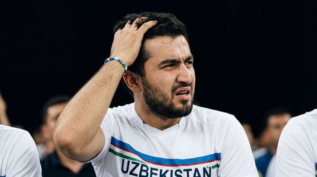 Uzbekistan athlete running hand through hair, looking tense on bench during match
