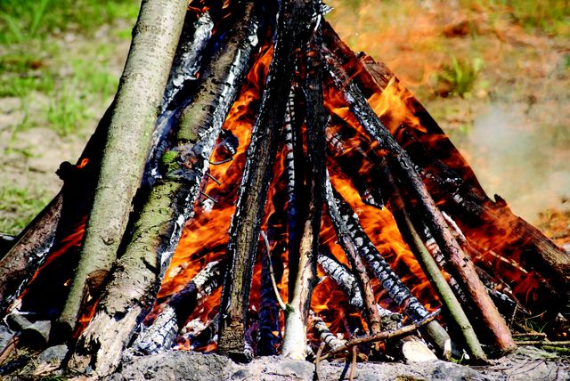 Close-up view of bonfire burning with logs in outdoor wilderness. Flames are consuming the wooden logs, creating an intense heat source. Great for use in topics involving outdoor activities, camping experiences, survival skills, and forestry. Ideal for articles, blogs, promotional materials related to nature and outdoor adventures.