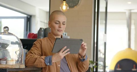 Bald woman standing at cafe counter holding tablet, checking orders in modern coffeehouse
