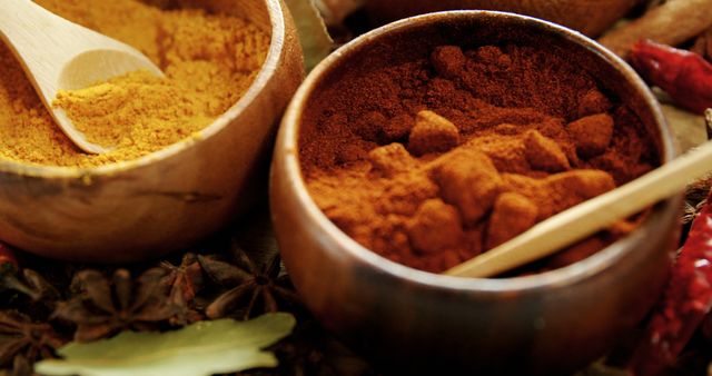 Close up of wooden bowls containing vibrant powders of turmeric and red chili pepper. Ideal for use in food blogs, culinary websites, recipe books, and organic spice advertisements.