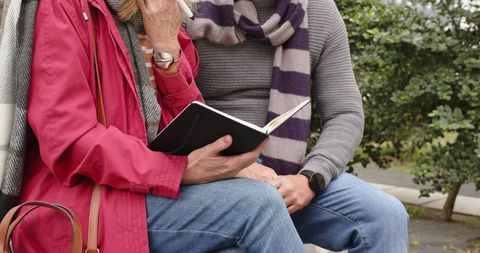 Senior couple writing in notebook on park bench planning retirement and travel