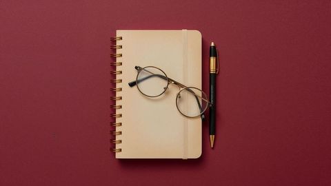 Notebook with glasses and pen on red background