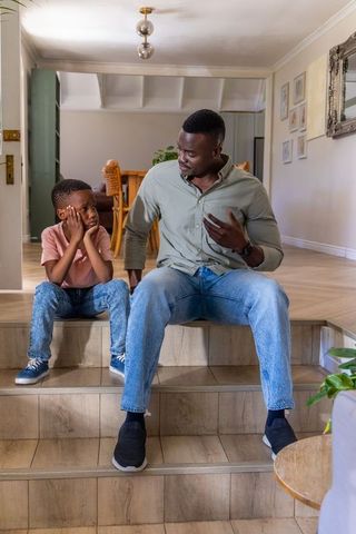 African american father explaining to son while sitting on tiled steps at home