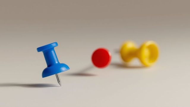 Blue pushpin balanced on surface with colorful pins in background