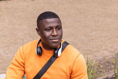 Young african american man sitting in urban plaza wearing headphones and orange sweatshirt