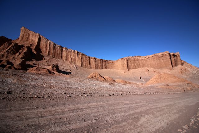 Dramatic red rock cliff formation under clear blue sky, emphasizing the geological wonders of arid desert landscapes. Useful for educational material on geology, travel articles showcasing scenic desert destinations, or inspirational natural landscape photography.