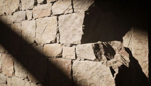 Warm sunlight catching textured granite masonry wall with diagonal shadow and jutting ledge