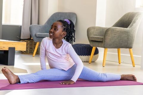 African american girl practicing middle split on purple yoga mat at home for flexibility