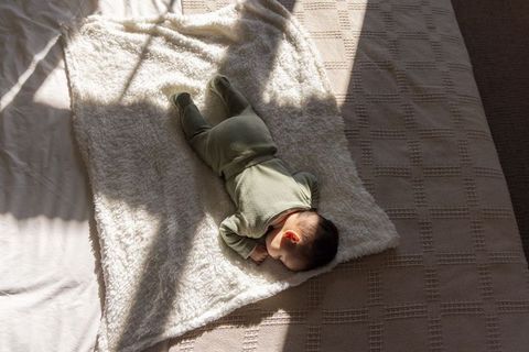 Sunlit newborn girl sleeping on plush blanket with soft window shadows and cozy warmth