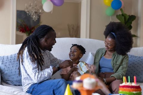 African american family celebrating child birthday at home with gift, cake and balloons
