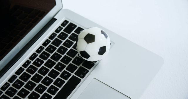 This image shows a small soccer ball placed on a laptop keyboard, symbolizing the intersection of sports and technology. Ideal for articles or blogs on sports digitalization, tech-savvy athletes, or online sports management. Visual could be useful in presentations related to modern workspaces and technology integration in sports.