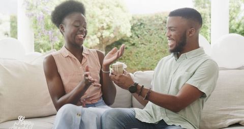 Joyful Young Couple Exchanging Gifts on Cozy Couch