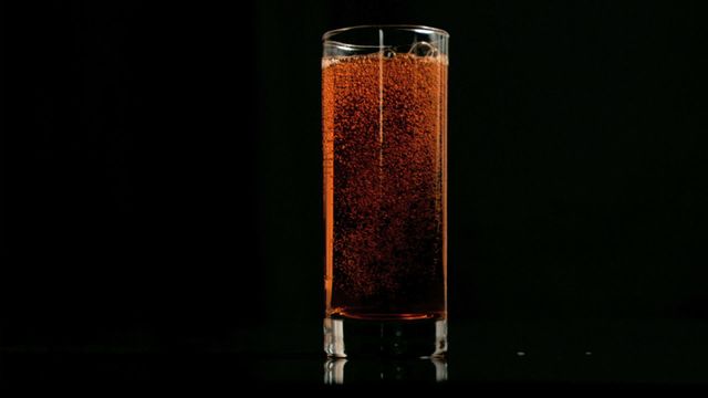 A close-up view of an amber-colored fizzy drink bubbling in a tall glass. The dark background emphasizes the effervescence and captures the dynamic nature of the carbonation in super slow motion. Perfect for use in advertising refreshing beverages, soda promotions, or illustrating the qualities of carbonated liquids in culinary and drinking content.