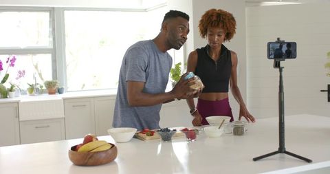 African american couple cooking healthy breakfast filming recipe with smartphone tripod