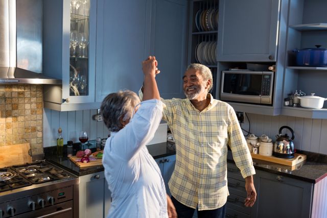 Senior couple enjoying a joyful moment dancing together in their kitchen. Ideal for illustrating themes of love, happiness, and vibrant senior living. Perfect for use in advertisements, retirement planning, healthcare, and lifestyle blogs.