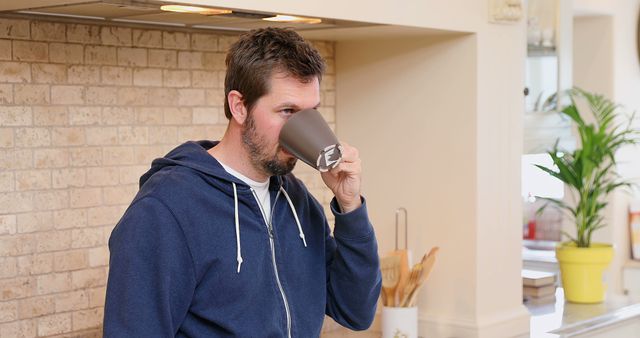 Man drinking coffee in a kitchen wearing a blue hoodie - Download Free Stock Images Pikwizard.com