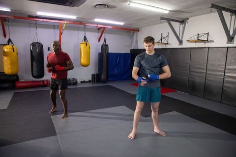 Sparring partners wrapping hands and warming up near heavy bags in martial arts gym