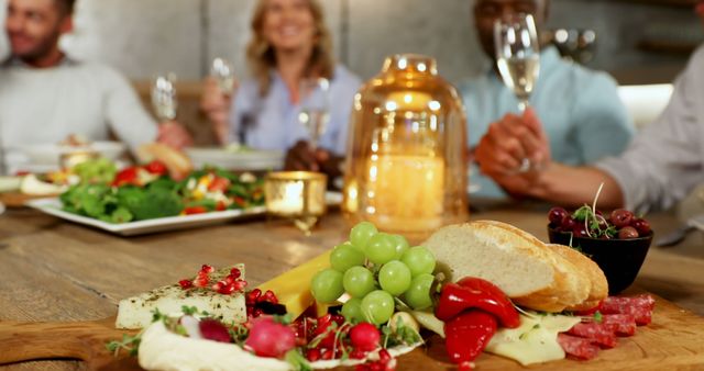 Group of friends sitting around a dining table enjoying dinner, featuring a charcuterie board with cheese, bread, grapes, and other appetizers. Perfect for illustrating social gatherings, dining, celebrations, and friendship. Suitable for use in food and beverage advertisements, party invitations, and social media content.