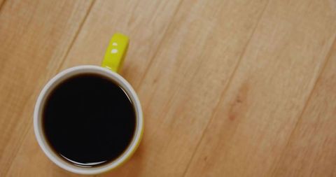 Top-down yellow mug holding black coffee on light wooden tabletop with copy space