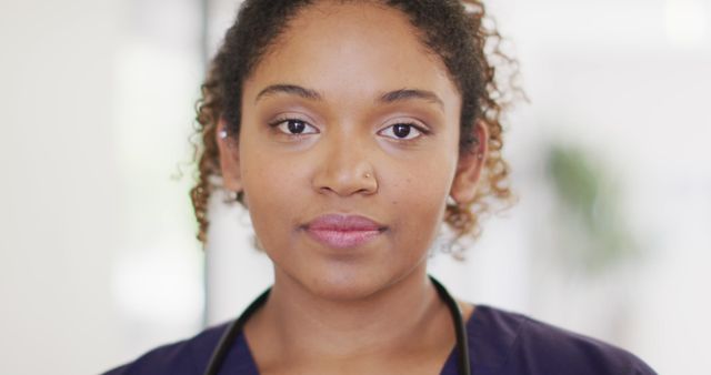 Young female healthcare professional in scrubs and stethoscope standing in hospital. Ideal for healthcare promotions, medical advertisements, professional profiles, or diversity in healthcare imagery.
