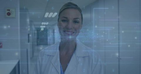 Smiling female doctor in lab coat standing in hospital hallway with digital data overlay